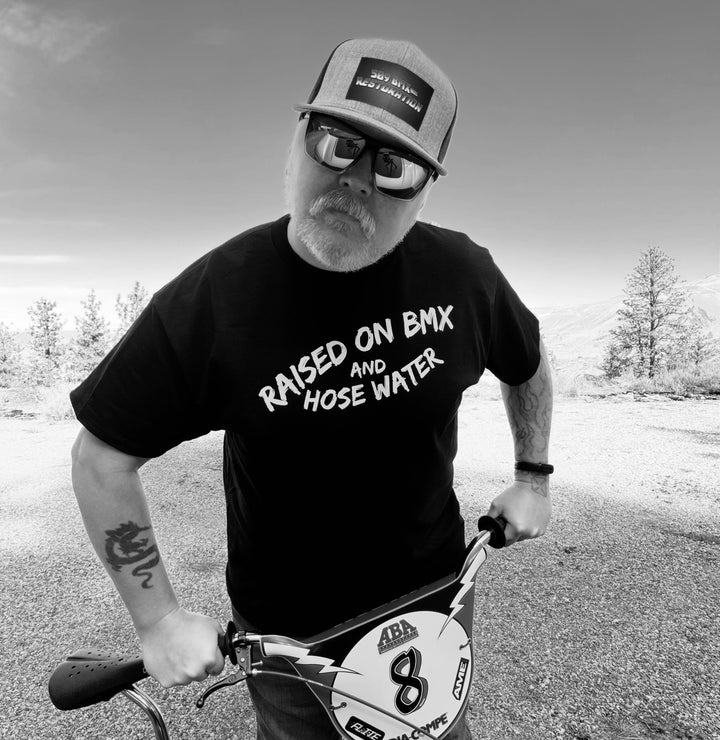 T-shirt made by 509 bmx restoration 50/50 Gildan t-shirt black with white writing that says Raised on BMX and Hose water. 